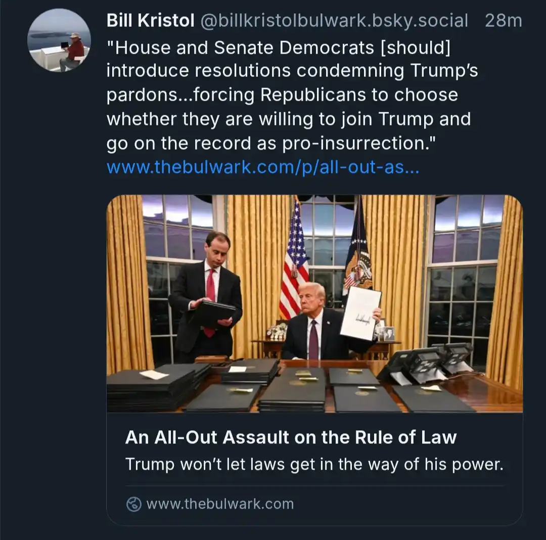 A screenshot of a social media post by Bill Kristol showing a photo of Donald Trump seated at a desk holding up a signed…