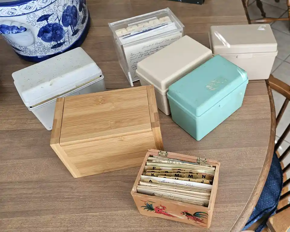 A wooden table holds several storage boxes of various materials and colors, including a bamboo box, a turquoise plastic box…