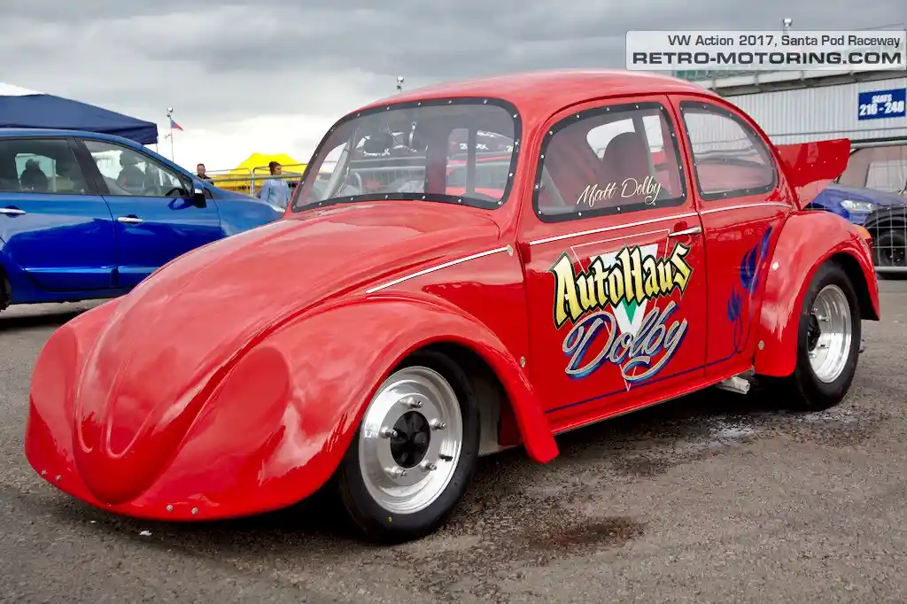 A red, modified Volkswagen Beetle race car with 'AutoHaus Dolby' and 'Matt Dolby' written on its side and window, parked at…
