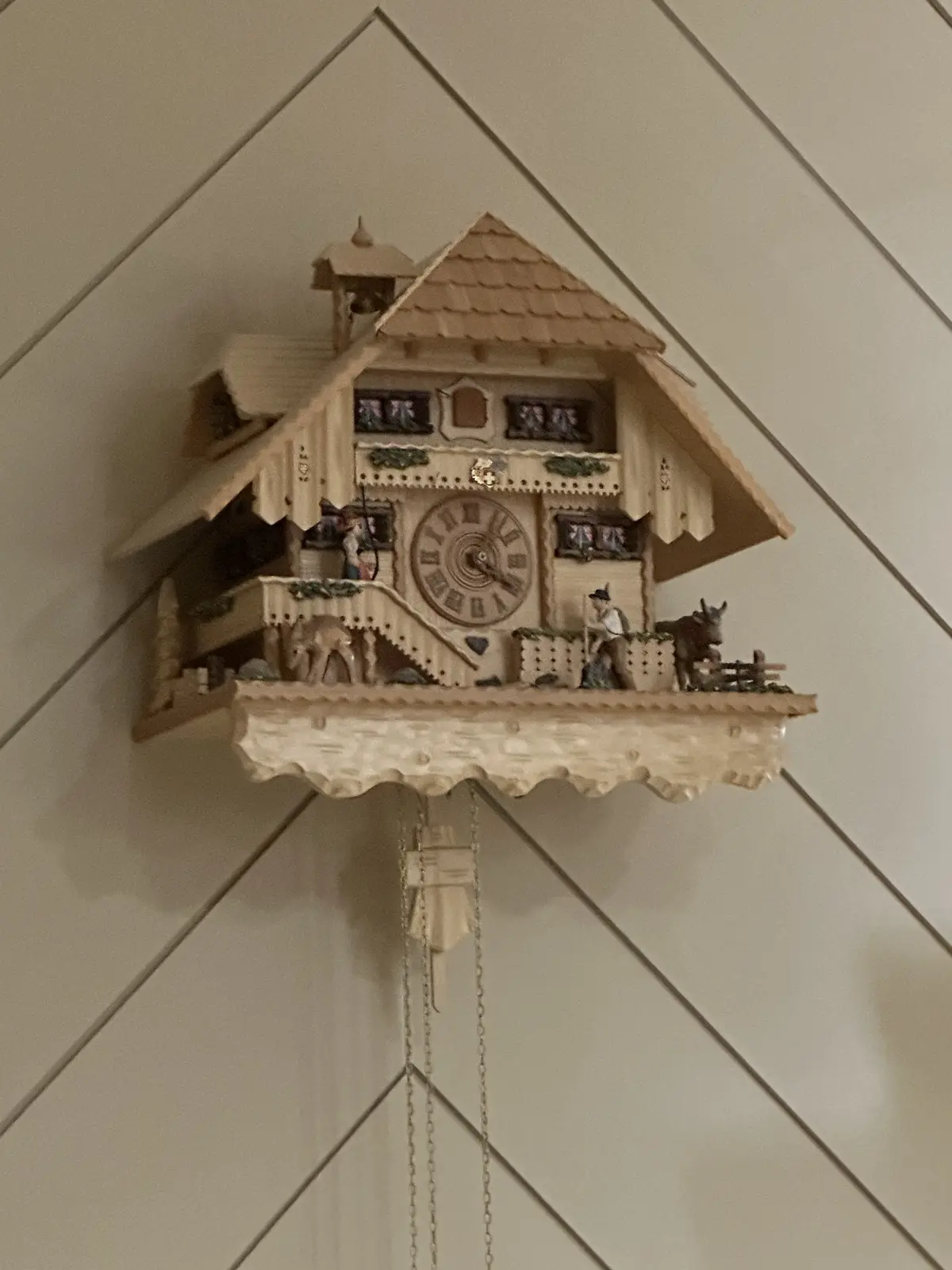 A traditional wooden cuckoo clock with a house-like structure, featuring a central clock face, figurines of people and…