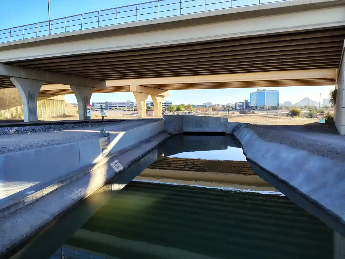 A photo of a concrete canal under a highway overpass, with a small amount of water and a stop sign visible on the left side…