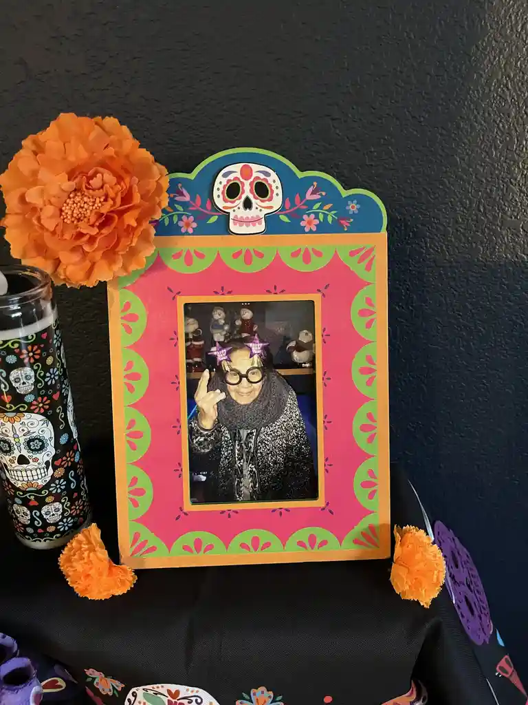 A vibrant Day of the Dead altar features a photo of an elderly woman wearing glasses and festive star-shaped headbands…