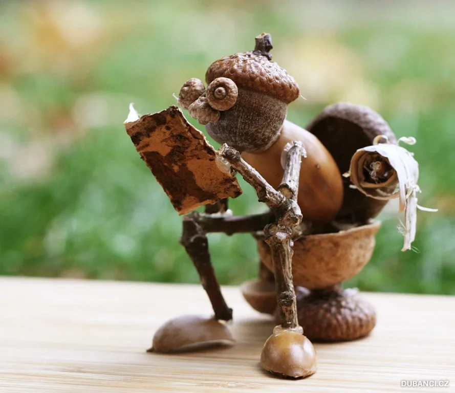 A whimsical sculpture made of acorns, twigs, and other natural elements depicts a tiny figure sitting on a wooden surface…