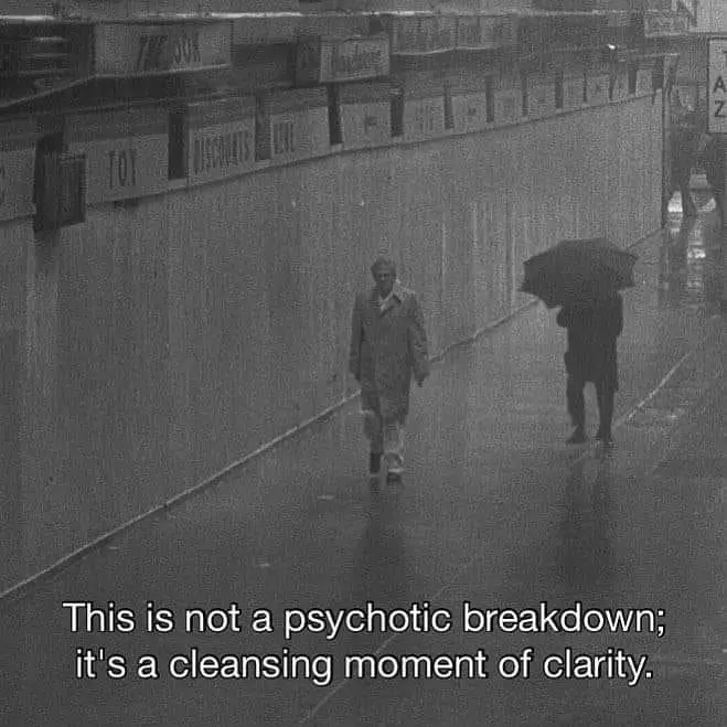 A grainy black-and-white photo shows two people walking down a wet, enclosed urban walkway. One person in a trench coat…