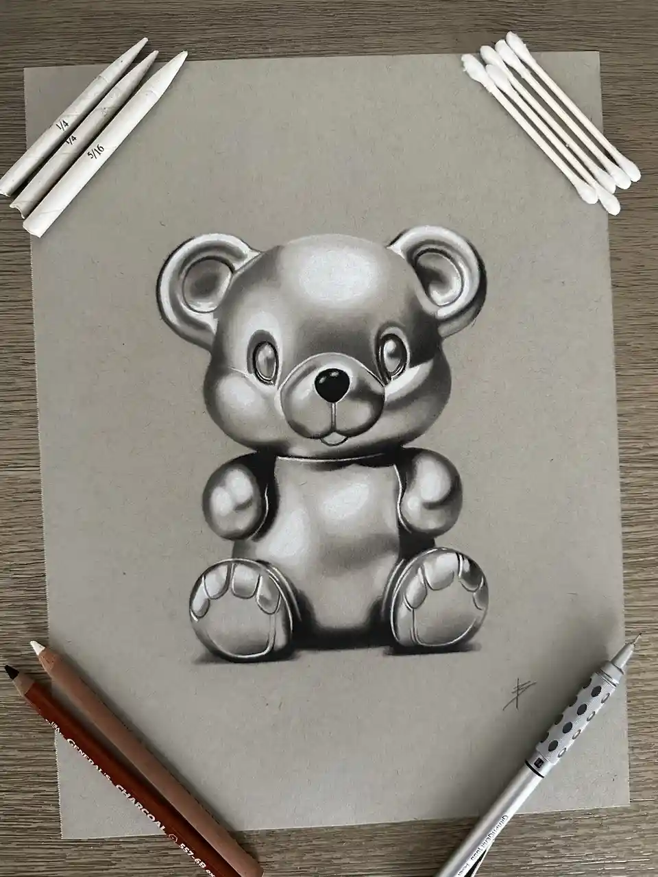 A highly detailed, realistic pencil drawing of a cute teddy bear on textured paper, surrounded by art supplies including…