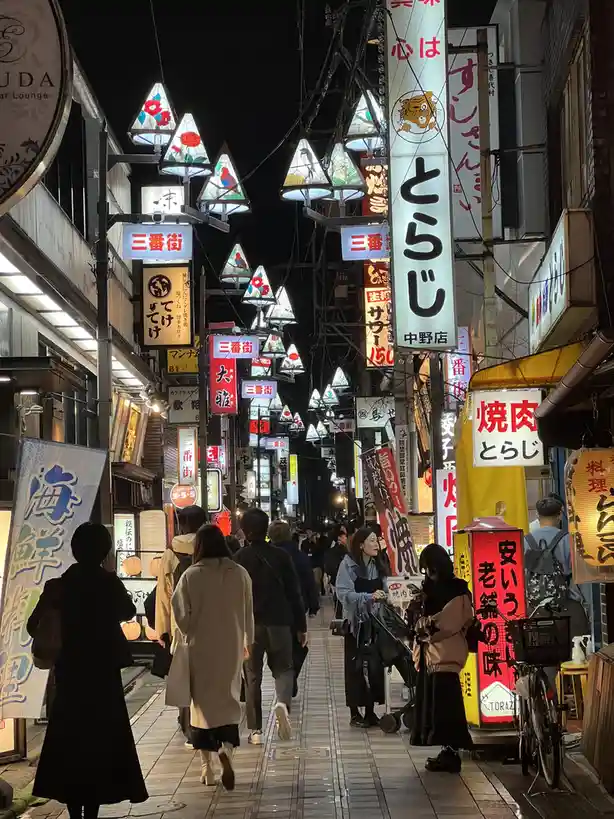 A bustling, narrow Japanese street at night, crowded with pedestrians walking under a dense canopy of glowing, colorful…