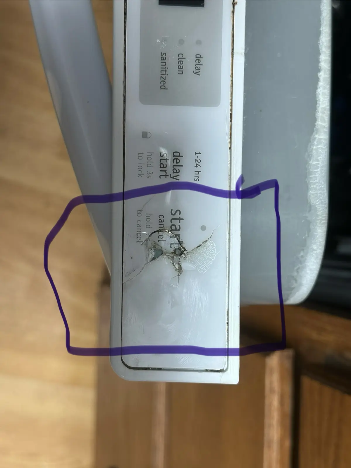 A close-up of a white appliance control panel with visible physical damage—a cracked and chipped area around the 'start'…