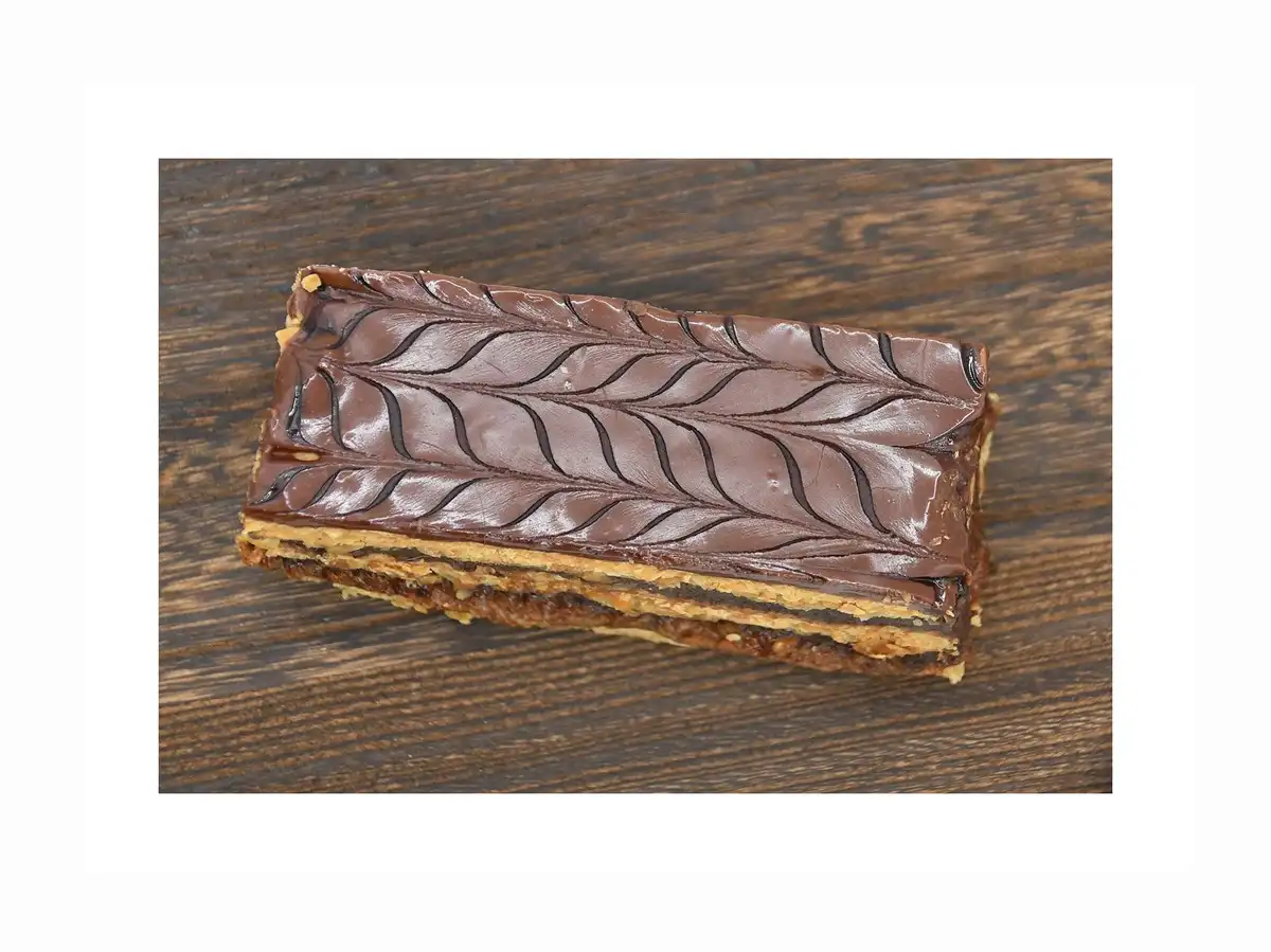 a rectangular chocolate-covered pastry with a glossy surface and wavy lines resembling tire treads sits on a dark wooden…