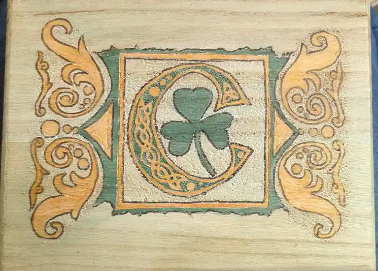 A hand-painted wooden plaque features a central green four-leaf clover inside a Celtic-style circular frame, surrounded by…
