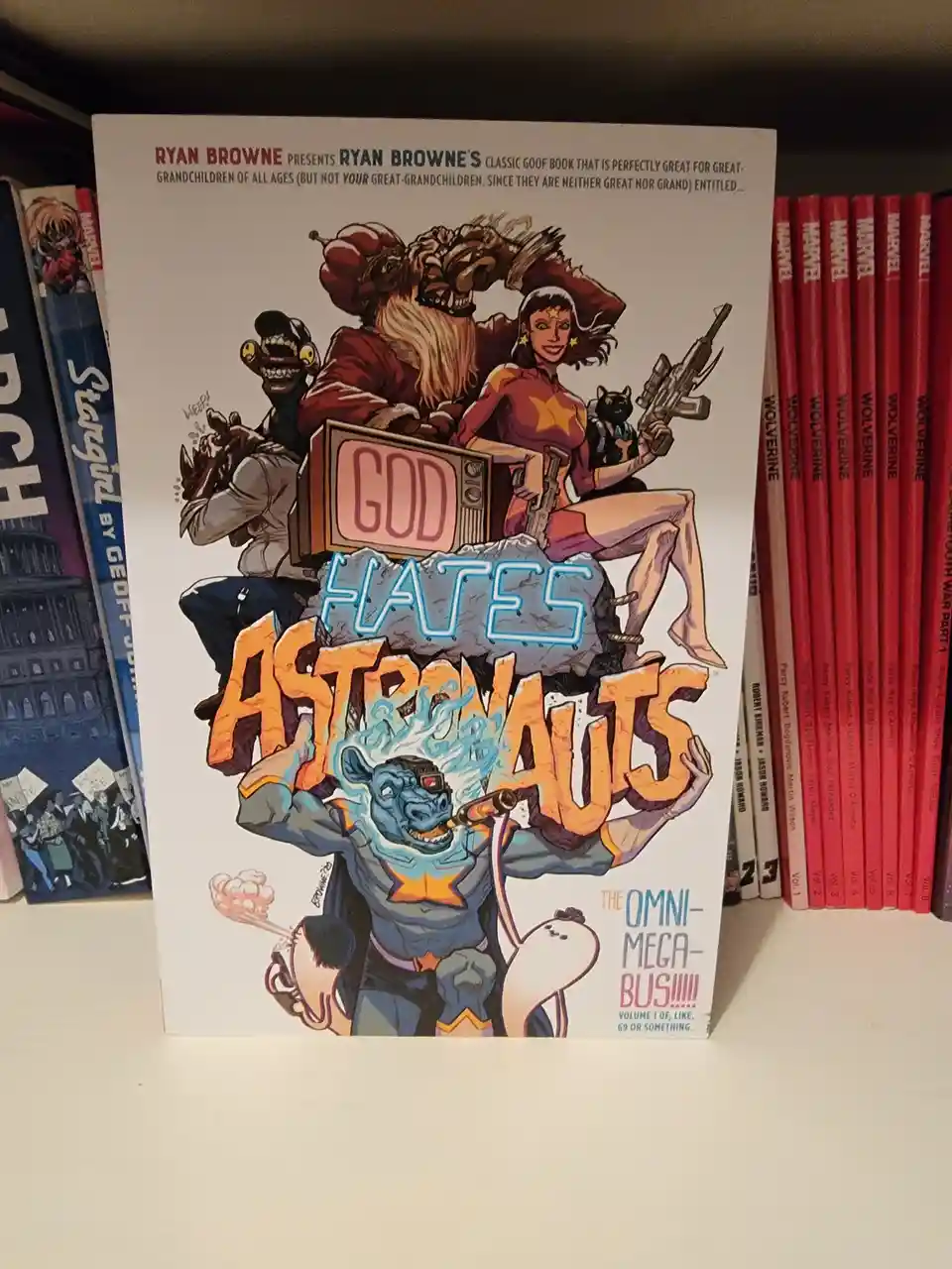 A comic book titled 'God Hates Astronauts' by Ryan Browne is displayed on a shelf, featuring a chaotic cover with cartoon…
