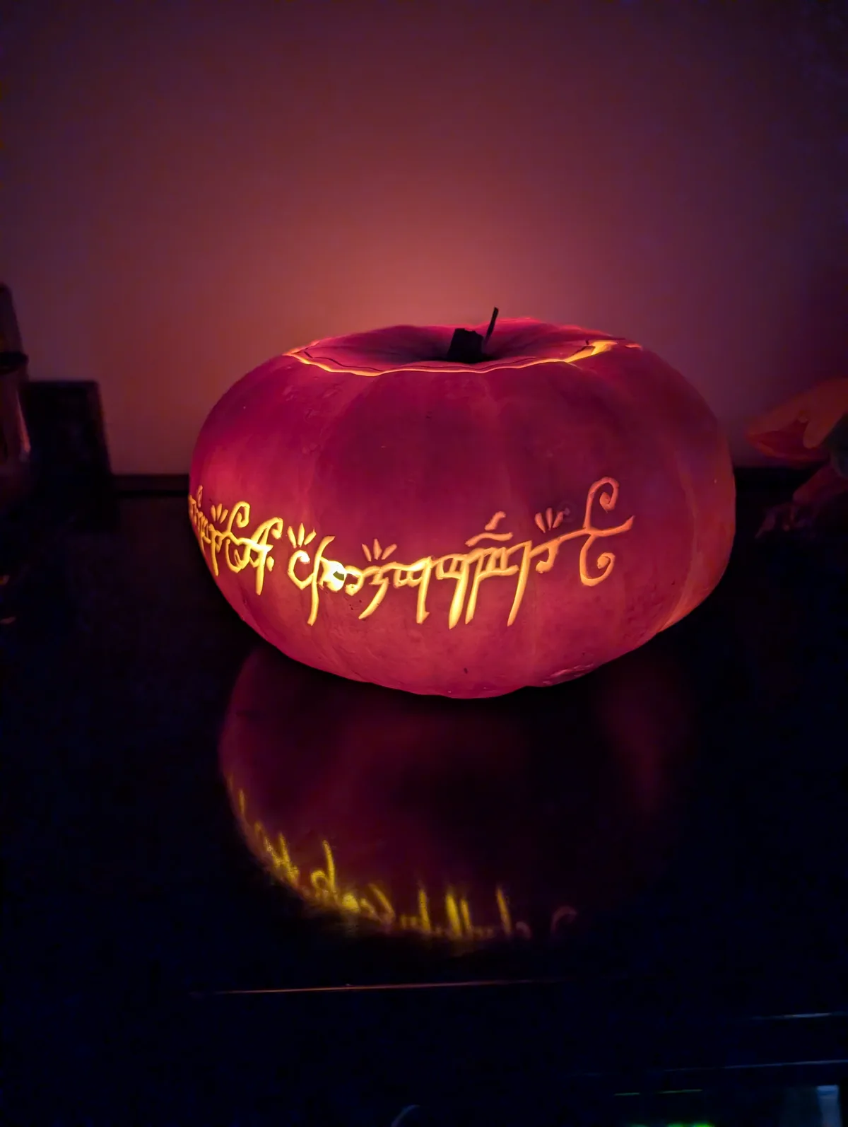 A carved pumpkin, illuminated from within, displays the phrase 'choose your own adventure' in glowing, cursive Elvish…