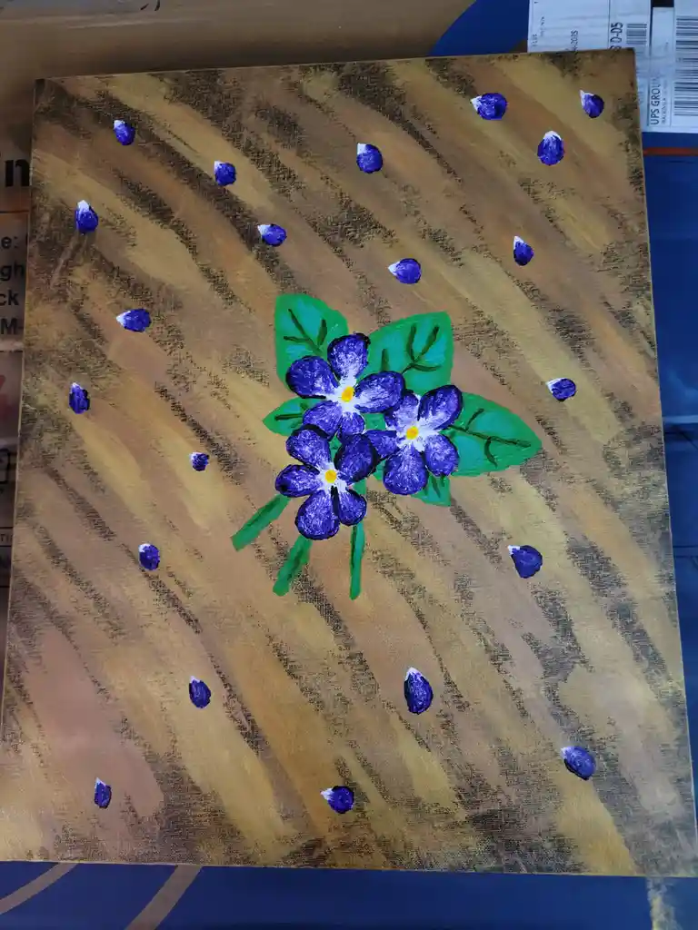 A hand-painted canvas depicts a cluster of purple flowers with green leaves and stems against a brown, textured background…