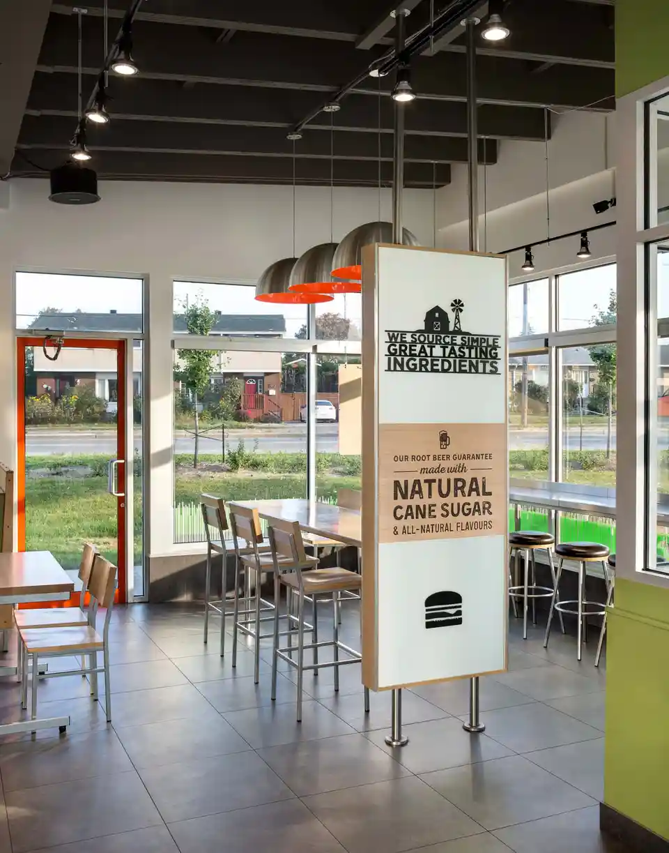 A tall, freestanding sign inside a modern restaurant or diner advertises 'WE SOURCE SIMPLE GREAT TASTING INGREDIENTS' and…