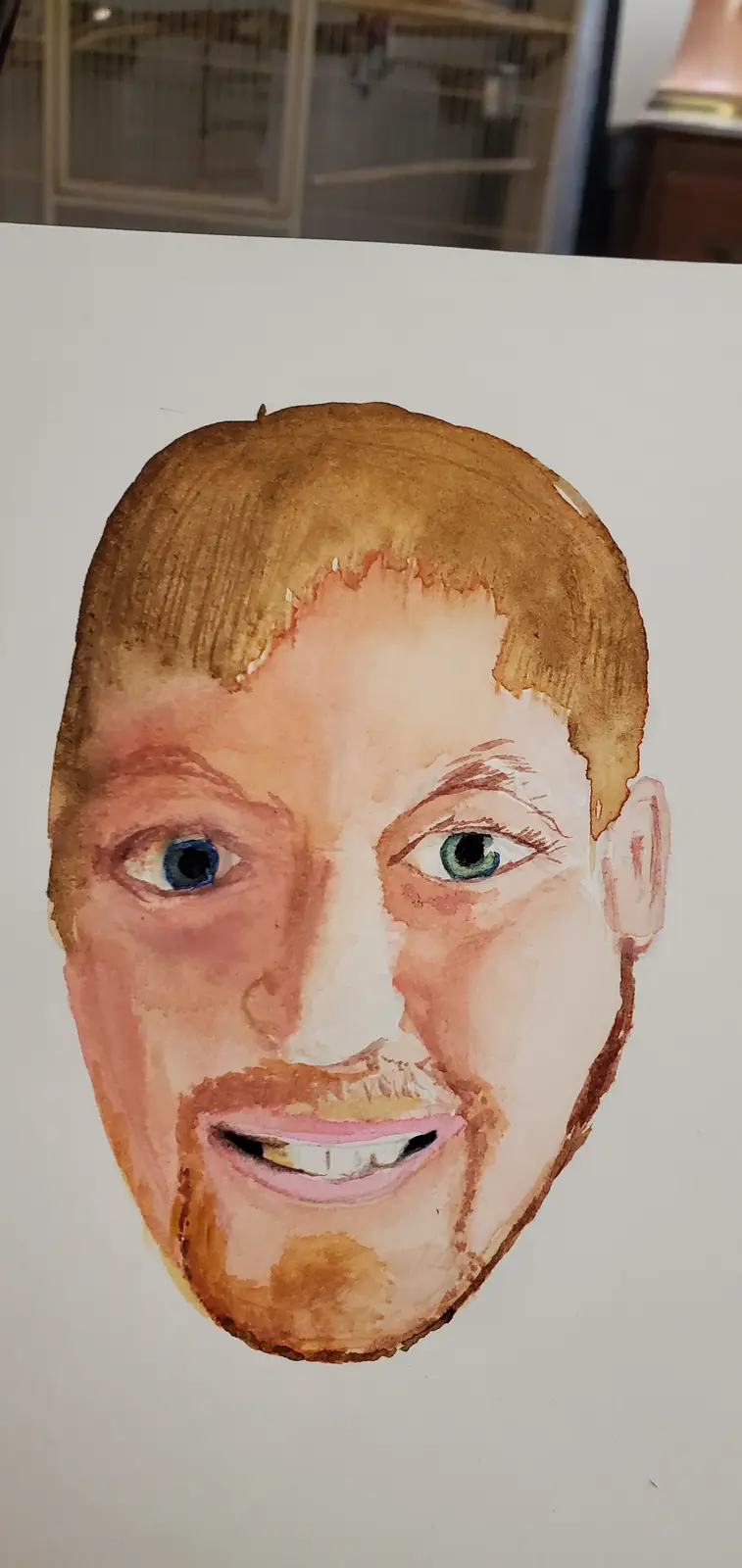 A watercolor portrait of a man's face on white paper, showing mismatched eyes (one blue, one green), uneven hair, and a…