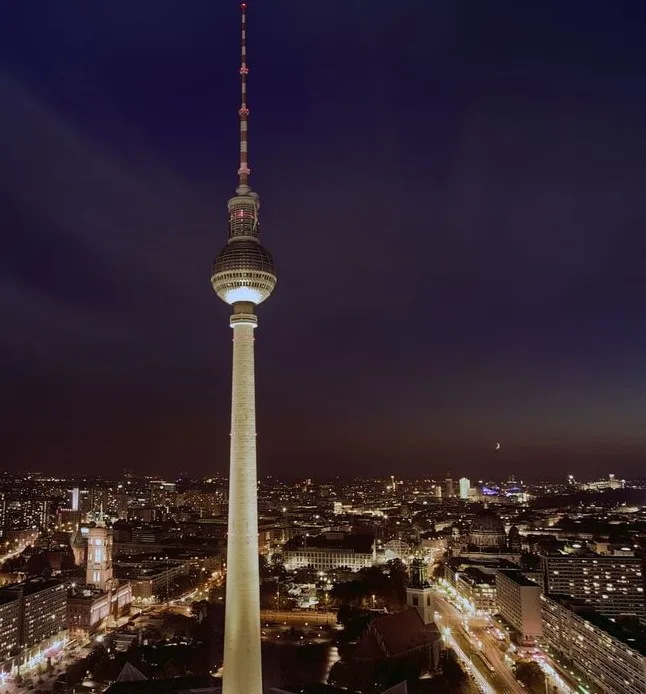 A nighttime photograph of the Berlin TV Tower (Fernsehturm) illuminated against a dark sky, with the cityscape lit below and…