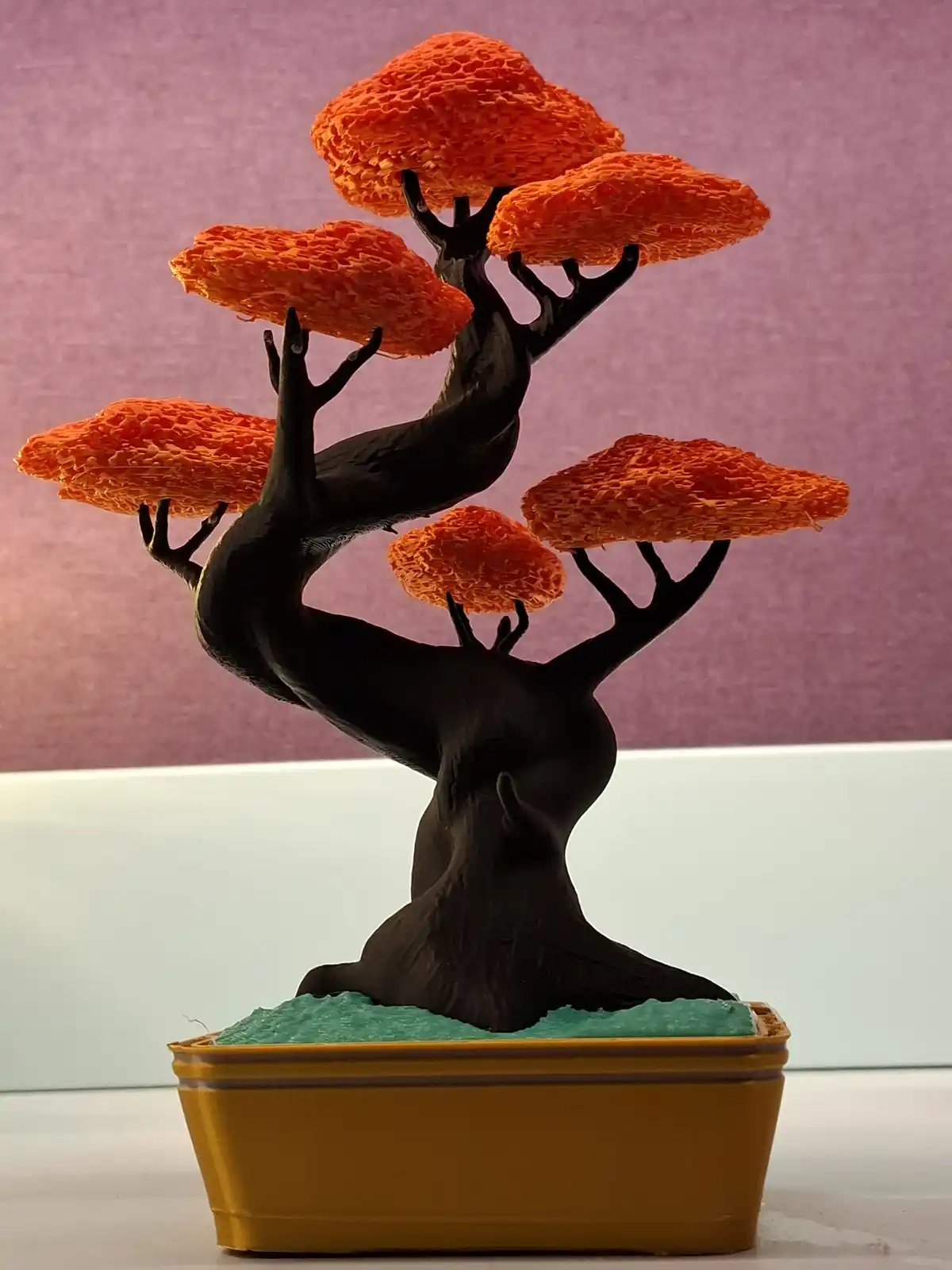 A stylized bonsai tree sculpture with a dark, gnarled trunk and bright orange, textured foliage, planted in a mustard-yellow…