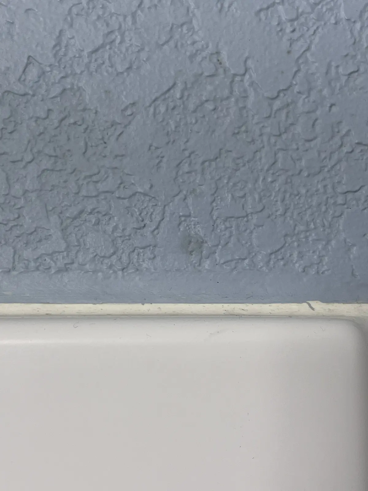 A close-up photo shows a textured, light gray wall meeting a white baseboard or bathtub edge; the overlaid text reads 'i'm…