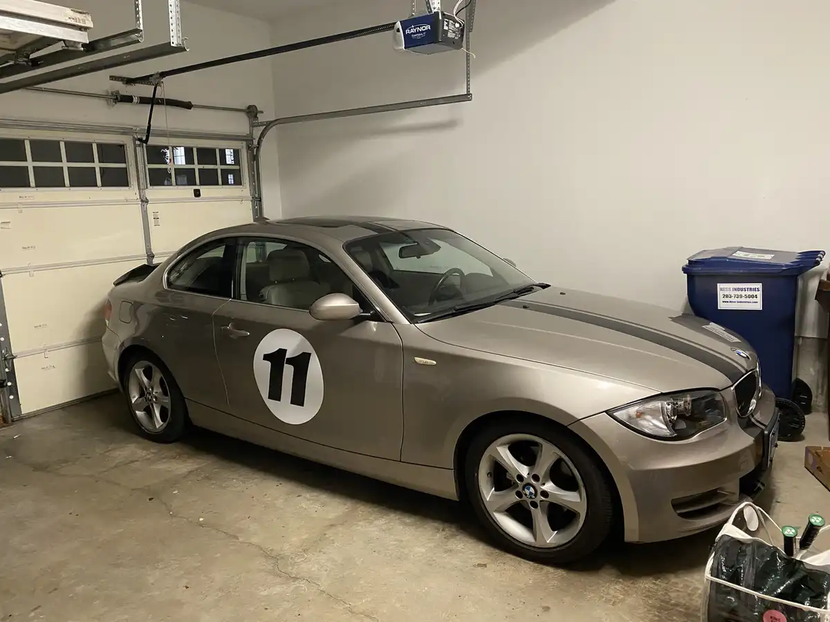 A silver BMW coupe is parked inside a residential garage, featuring a large white circular decal with the number 11 on its…