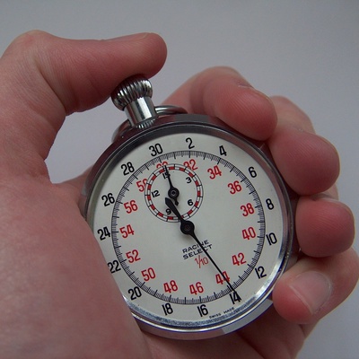 A hand holds a vintage-style analog stopwatch with a white face and red markings; the second hand points to 140, which is…