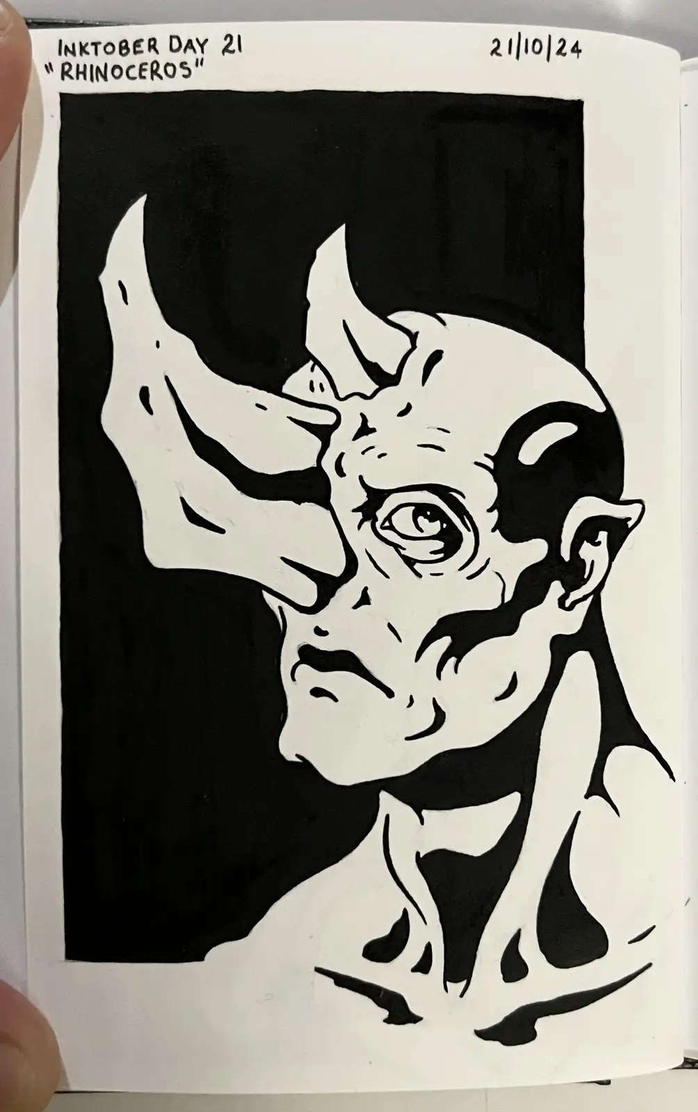 A black and white ink drawing of a demonic-looking creature with a large rhinoceros horn on its forehead, pointed ears, and…