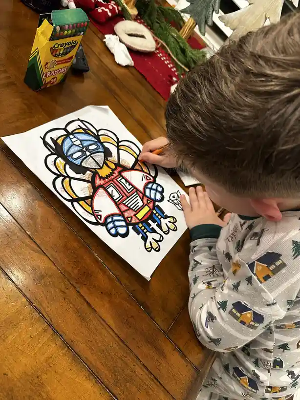 A young child is coloring a drawing of a turkey that has been creatively transformed to resemble the superhero Captain…