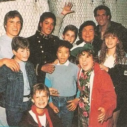 A group photo of Michael Jackson with several children and teenagers from the 1980s, some smiling, one making a silly face…