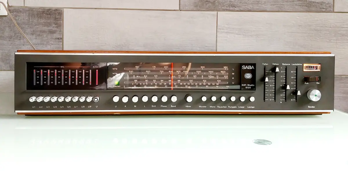 A vintage SABA HiFi Studio 8120 stereo receiver with a large tuning dial and multiple knobs, sitting on a white surface…