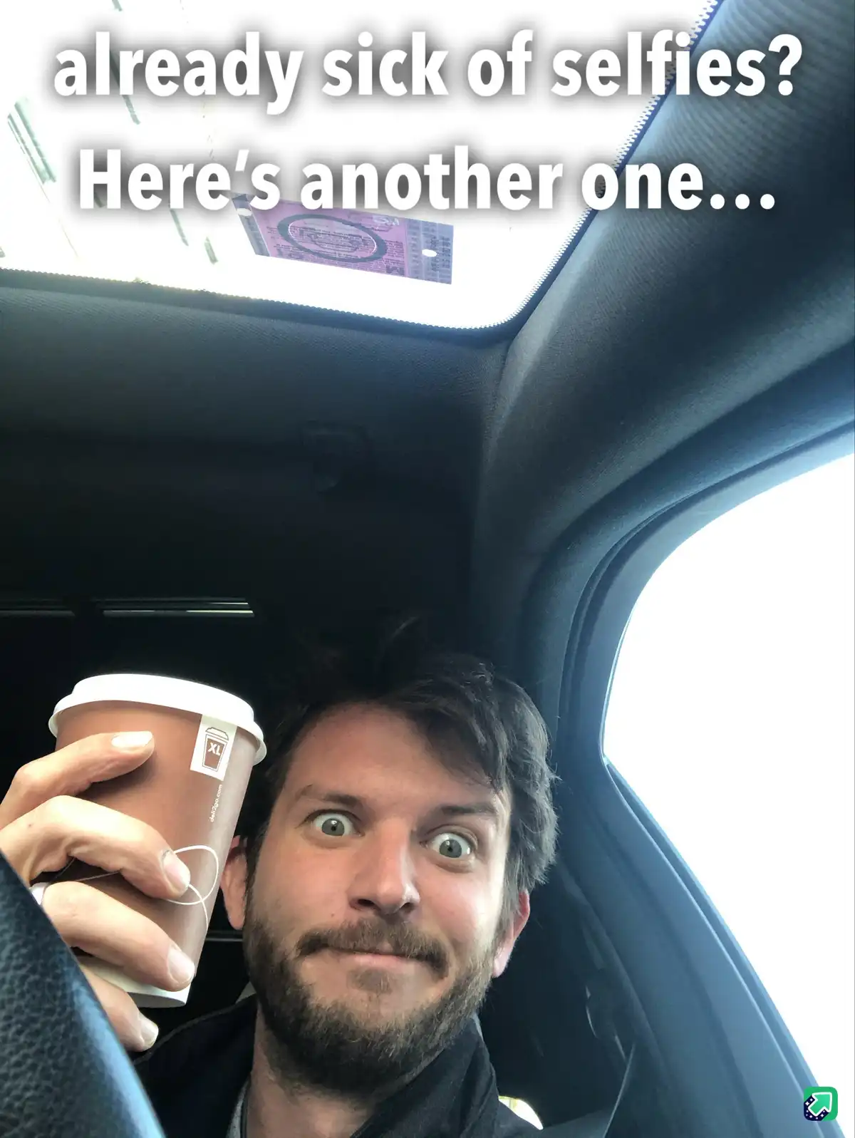 A man with a beard and wide eyes takes a selfie inside a car, holding a brown coffee cup with a white lid. The car's sunroof…