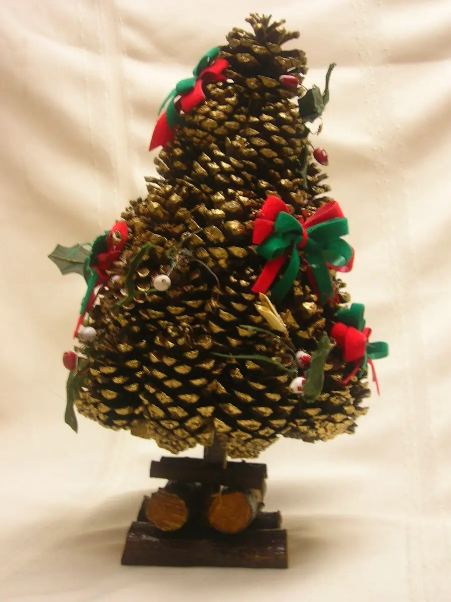 a decorative christmas tree made from a large, golden-painted pinecone, adorned with red and green bows, small holly leaves…