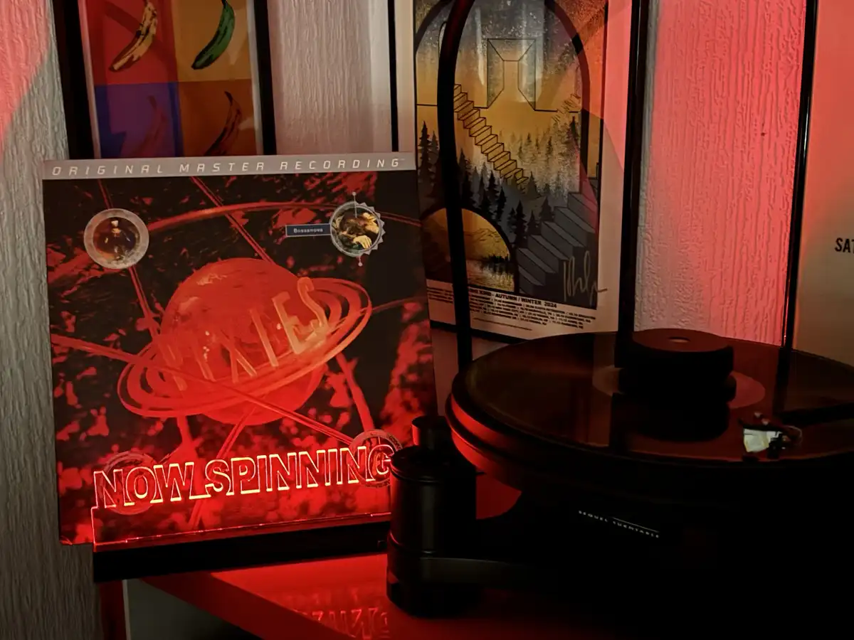 A vinyl record player with a record on it sits next to a framed album cover for 'Pixies' that reads 'ORIGINAL MASTER…
