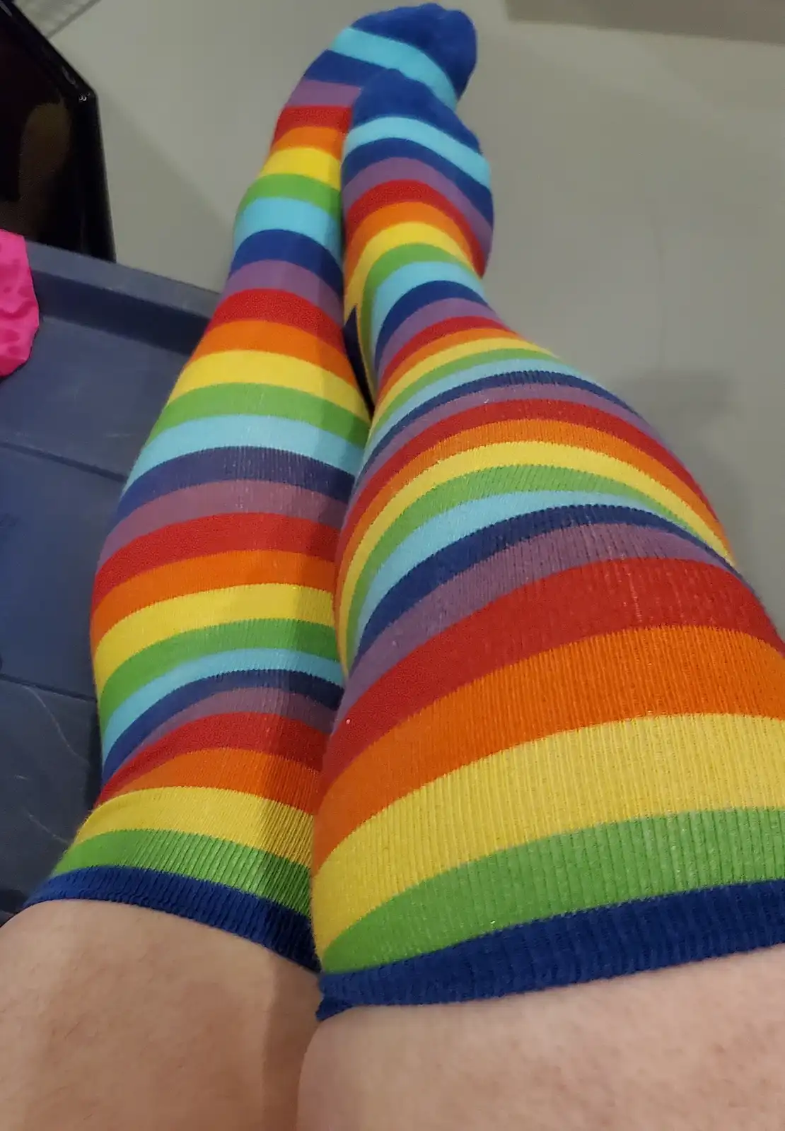 A close-up photo shows a person's legs wearing bright, rainbow-striped knee-high socks, with the feet pointing upward. The…