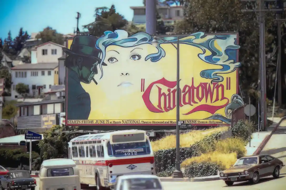 A vintage billboard advertising the 1974 film 'Chinatown' features a stylized illustration of a man in a fedora and a woman…
