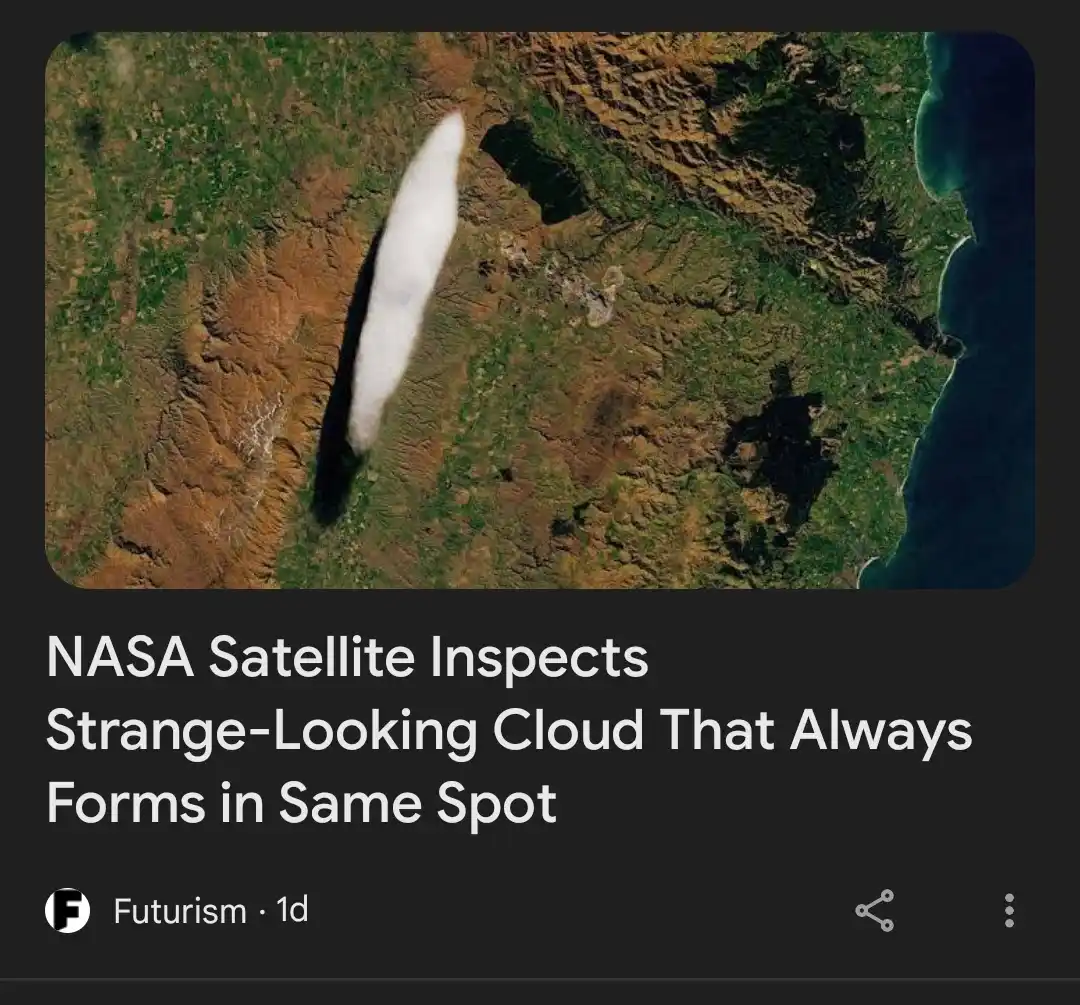 A satellite image shows a long, white, cigar-shaped cloud hovering over a rugged, green and brown landscape with a coastline…