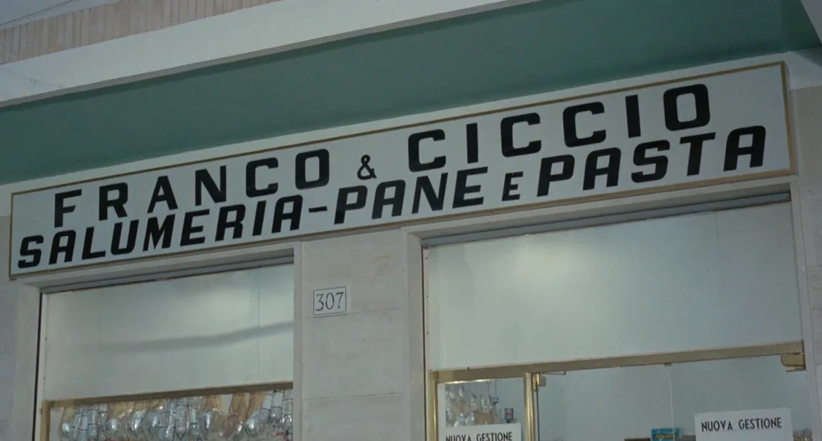 A storefront sign reads 'FRANCO & CICCCIO SALUMERIA-PANE E PASTA' in bold black letters on a white background. The shop…