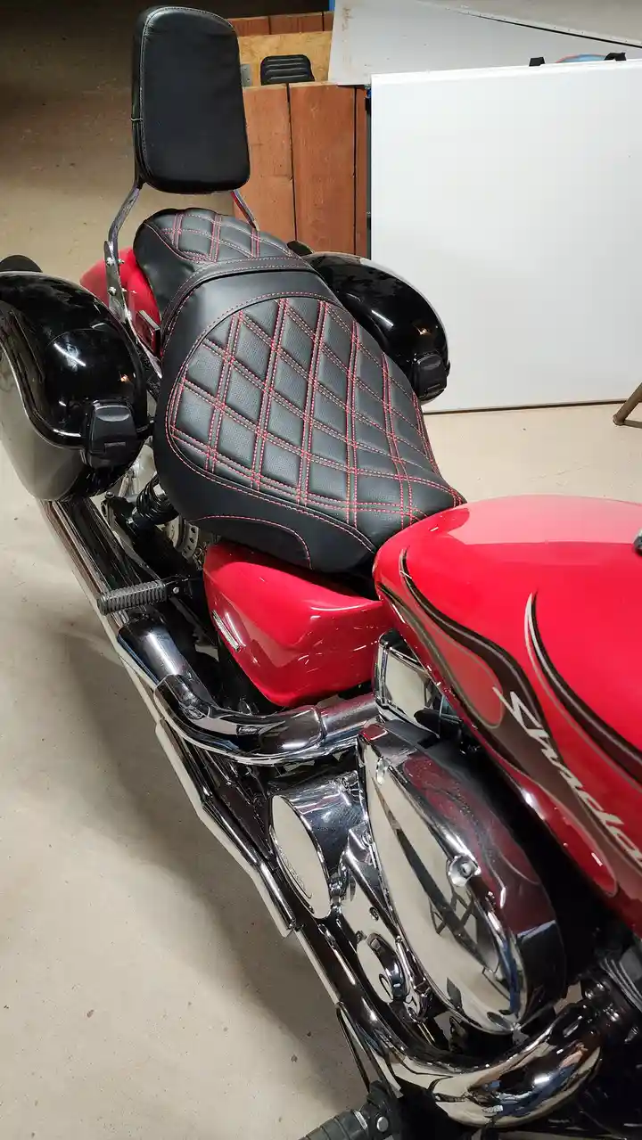 A close-up photo of a red and black motorcycle with a quilted black seat and red stitching, chrome exhaust pipes, and black…