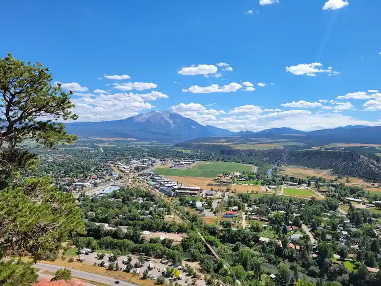 A scenic, high-angle photograph of a town nestled in a valley with mountains in the background under a bright blue sky with…