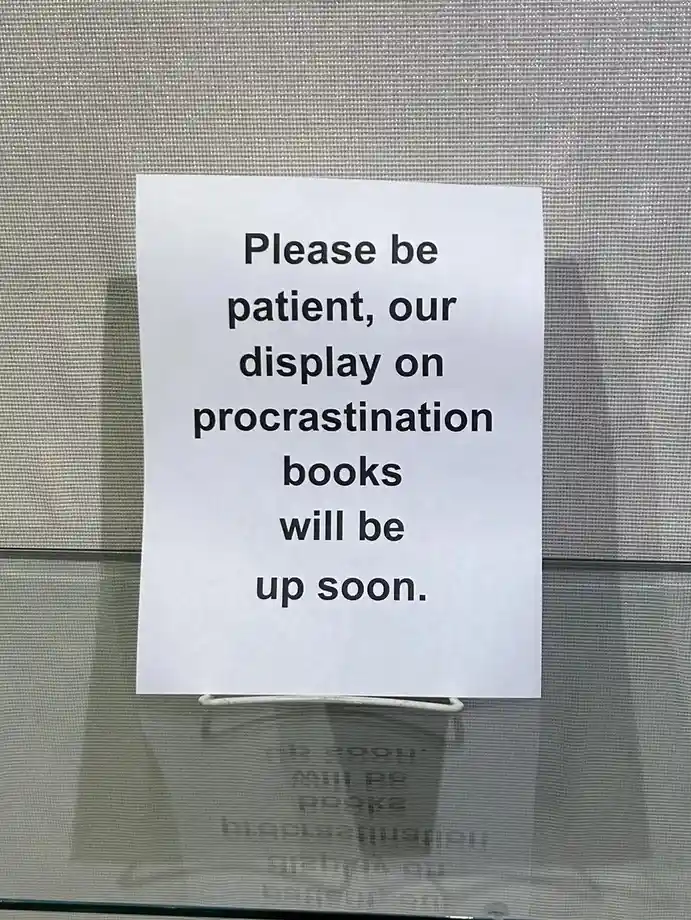 A white paper sign is taped to a glass surface with a textured gray background, displaying the text 'Please be patient, our…