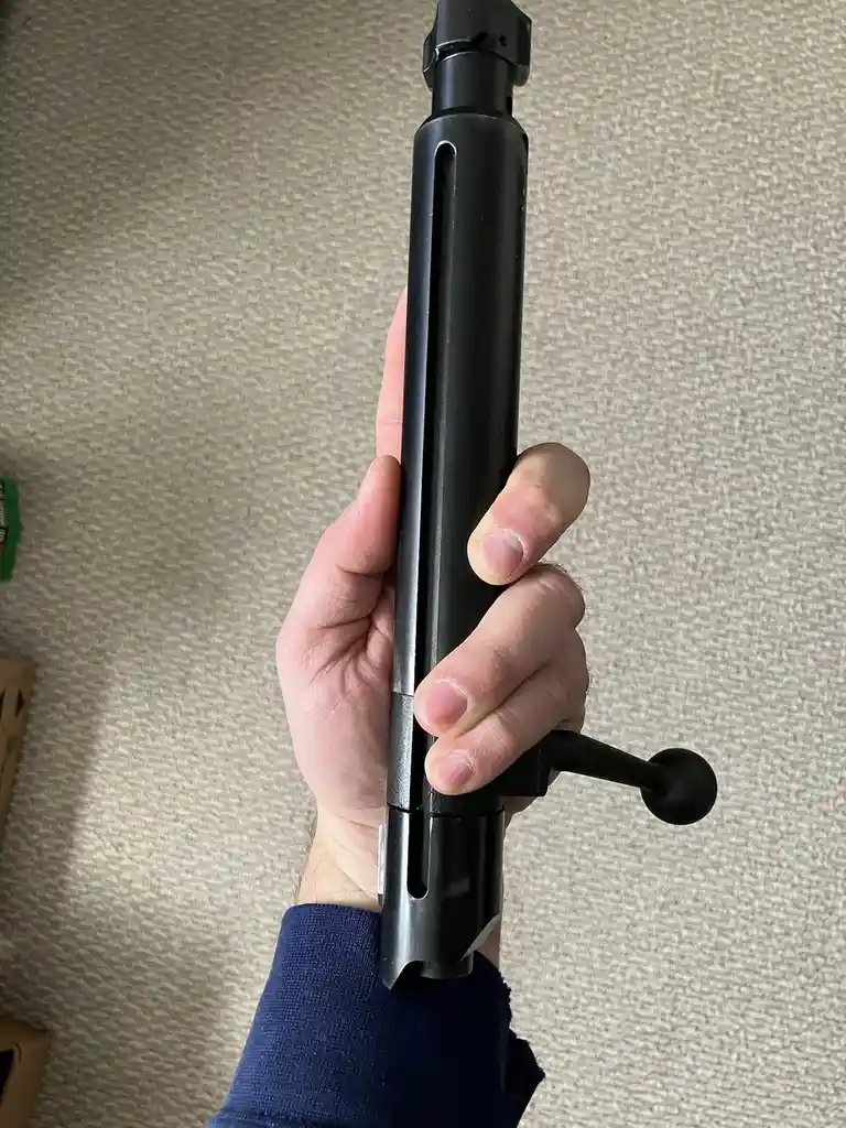 A person's hand holds a black, cylindrical object with a handle and a lever, resembling a rifle stock or a tool, against a…