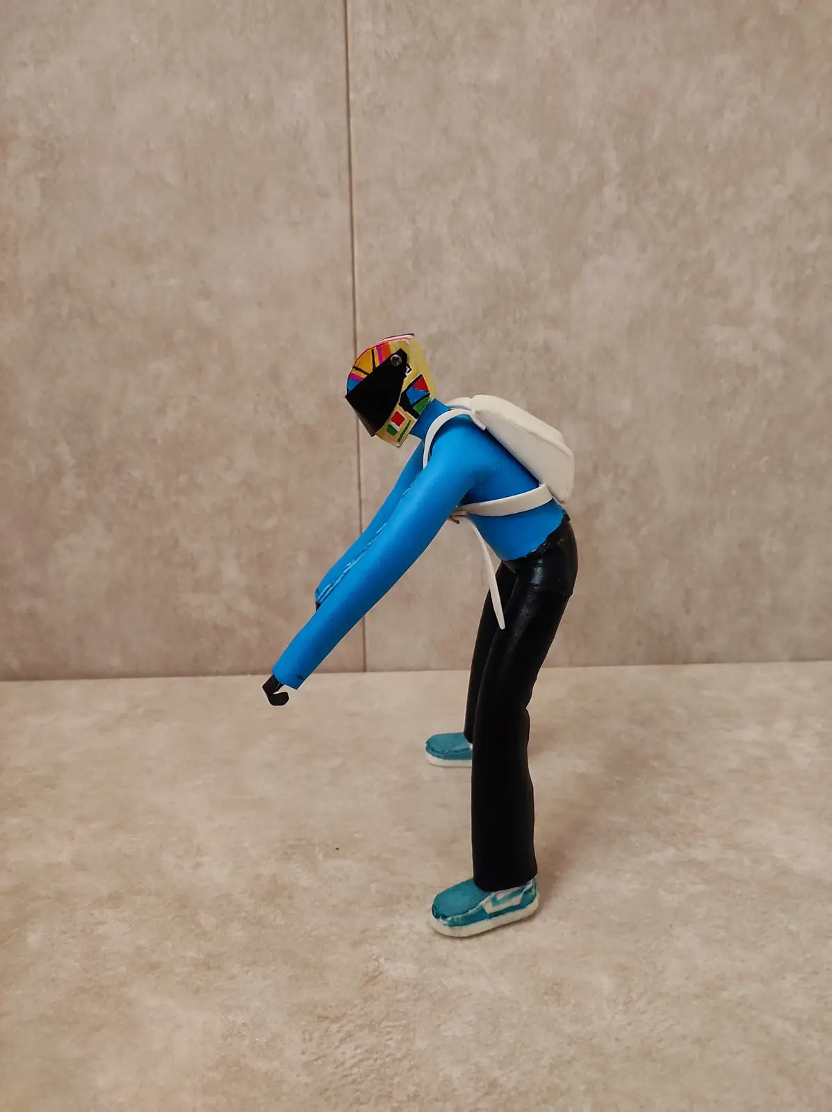 A handmade figurine of a blue Power Ranger with a colorful helmet and white backpack is bent over at the waist, reaching…