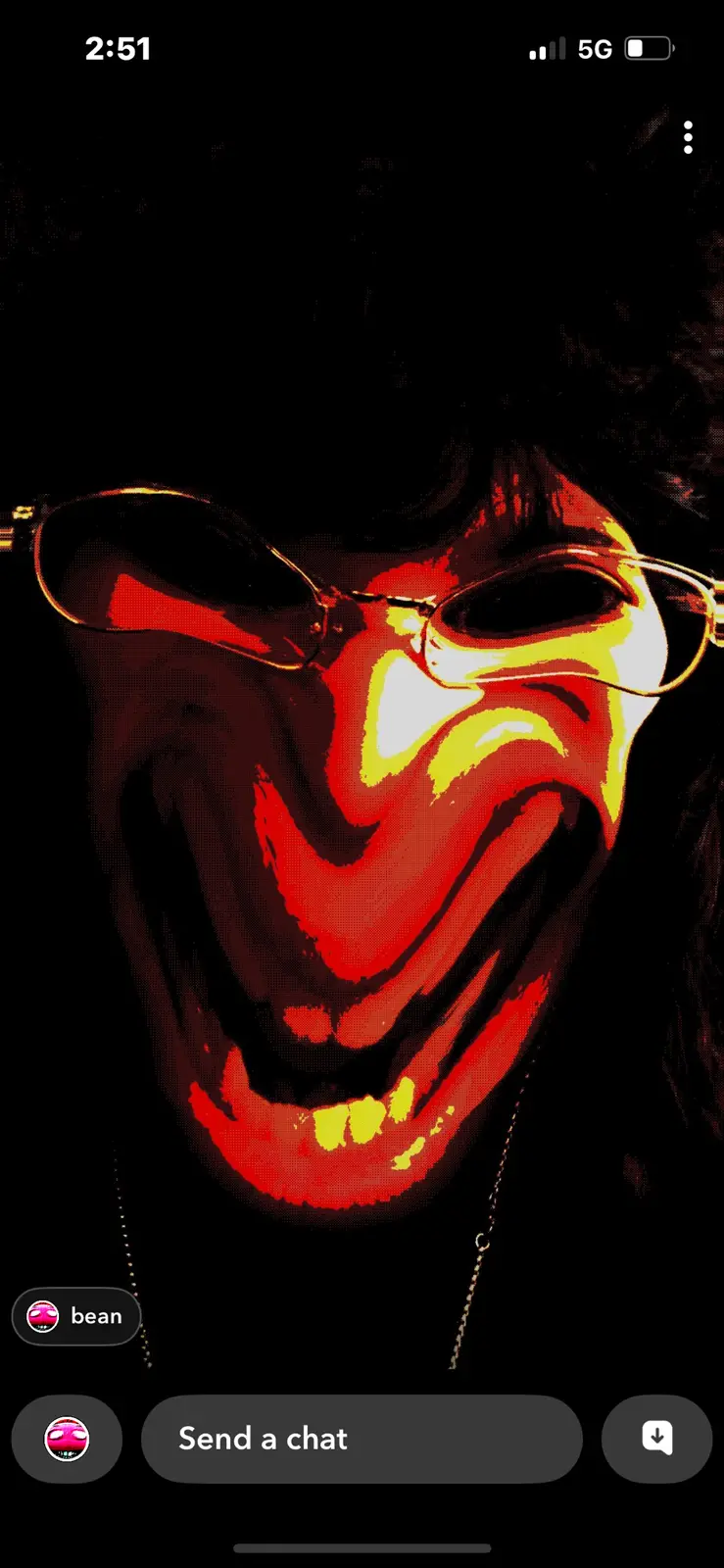 A stylized, high-contrast image of a person with a wide, unsettling grin, wearing glasses and a chain, set against a black…