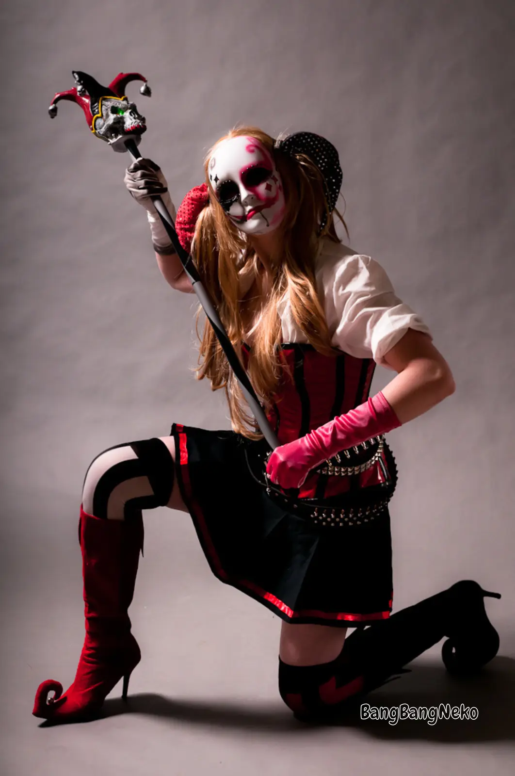 A person in a Harley Quinn cosplay, wearing a white face mask with red and black makeup, a red and black corset, a black…