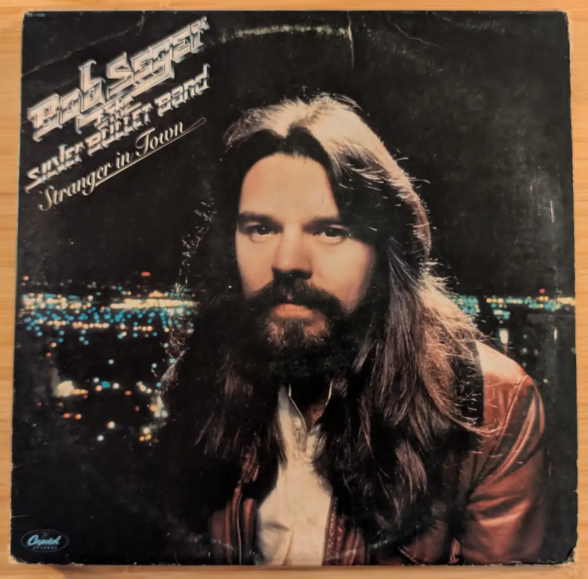 A vintage album cover for Bob Seger & The Silver Bullet Band's 'Stranger in Town,' showing a man with long hair and a beard…