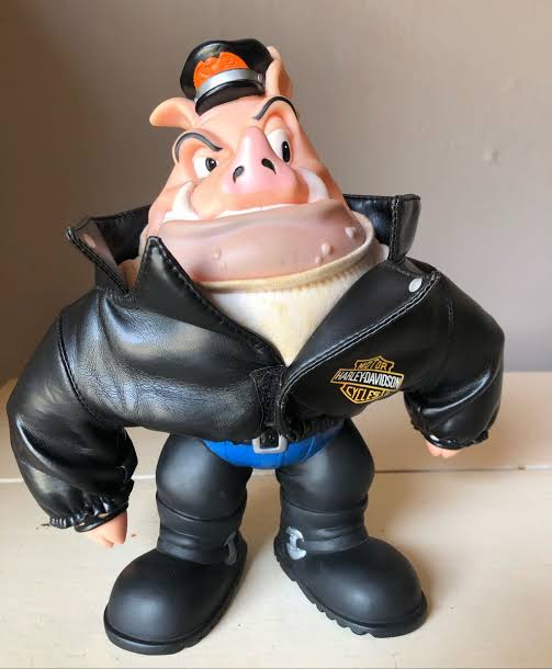 A plastic figurine of a cartoon pig wearing a black leather Harley-Davidson jacket, blue jeans, black boots, and a black cap…