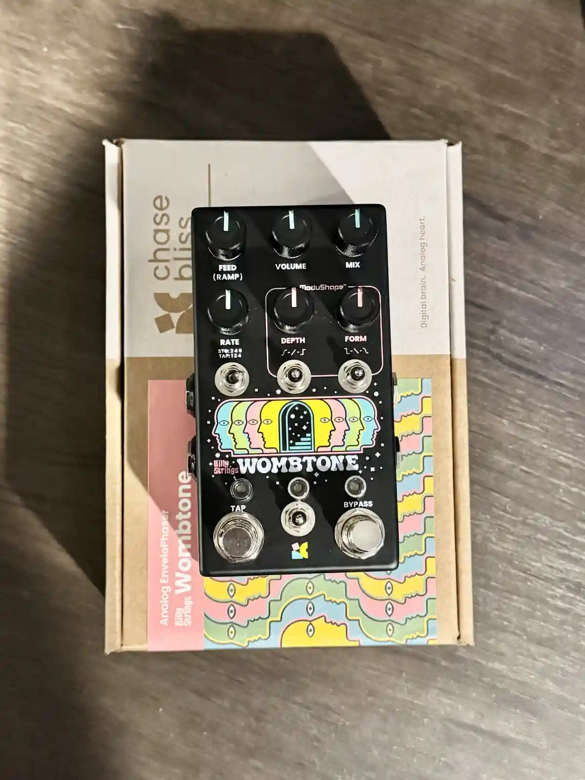 A black Chase Bliss Wombtone analog envelope phaser guitar pedal with colorful psychedelic artwork of repeating faces is…