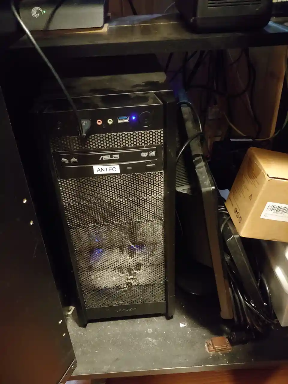 A dusty black desktop computer tower with a perforated front panel, where the mesh pattern forms the shape of a skull…