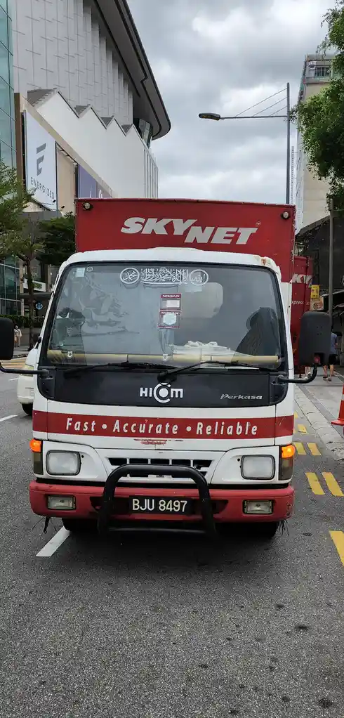 A red and white delivery truck with 'SKYNET' written in large white letters on its red cargo box. The front of the truck…