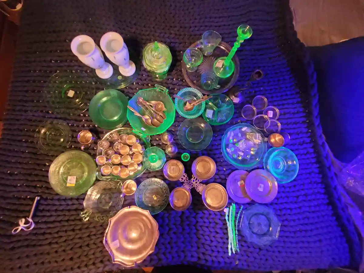 An overhead shot shows a large collection of vintage glassware, including green and blue plates, bowls, cups, and…