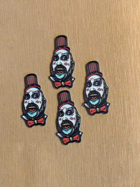 Four identical enamel pins featuring a cartoonish, grinning clown with a black beard, white face paint, red cheeks, a black…