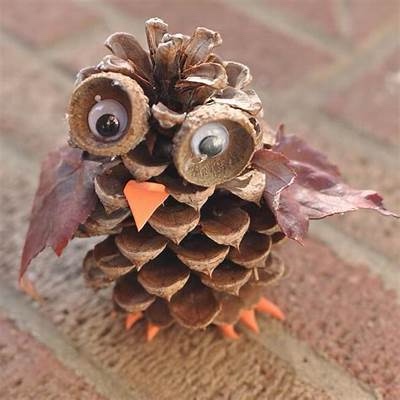 A pinecone is creatively decorated to resemble an owl, with two large googly eyes glued to its upper scales, a small orange…