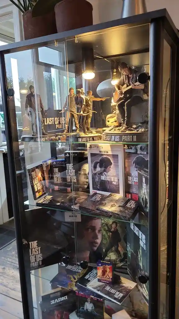 A glass display case filled with numerous collectible items from the video game 'The Last of Us Part II', including multiple…